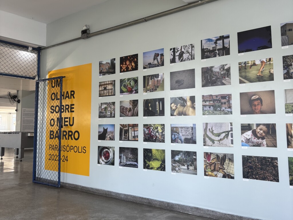 Panel de la exposición "Una mirada a mi barrio – Paraisópolis", con fotografías tomadas por estudiantes de Crescer Sempre, expuesto en el pasillo de una escuela.